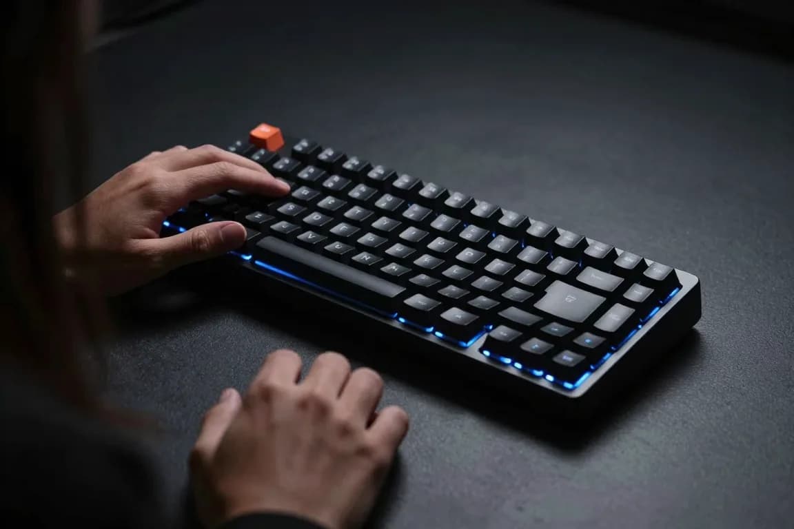 מבט מעל הכתף על ידיים מקלידות על מקלדת מכנית קומפקטית מוארת